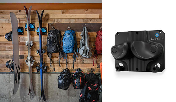 A snowboard and skis hanging on a wall mount display in a garage hanging with other outdoor gear.